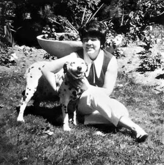 Photo of young woman sitting on grass with a spotted dog
